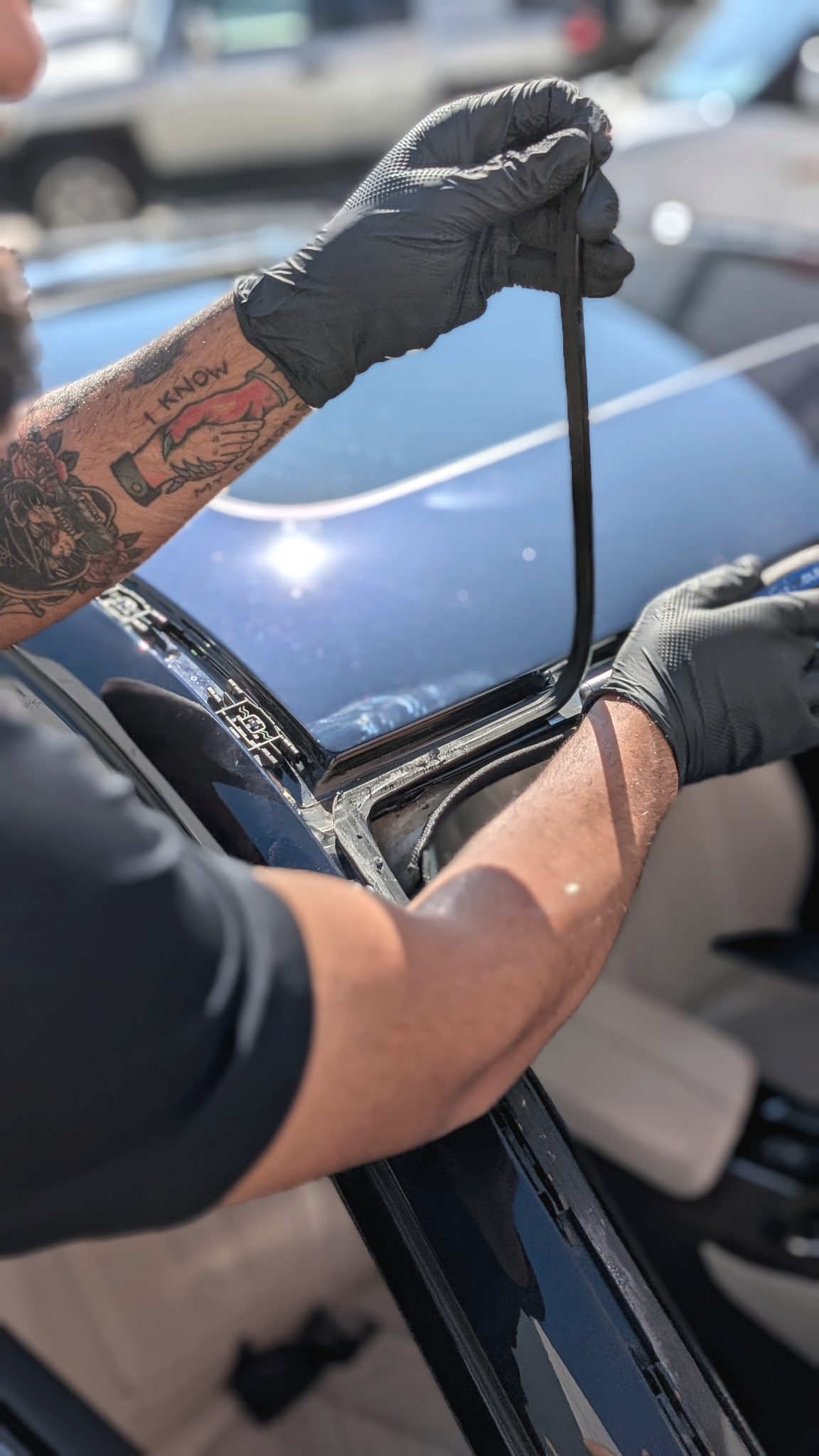 Gloved hands fitting a new windshield moulding on a car at a mobile appointment, pulling the seal into place in the sun